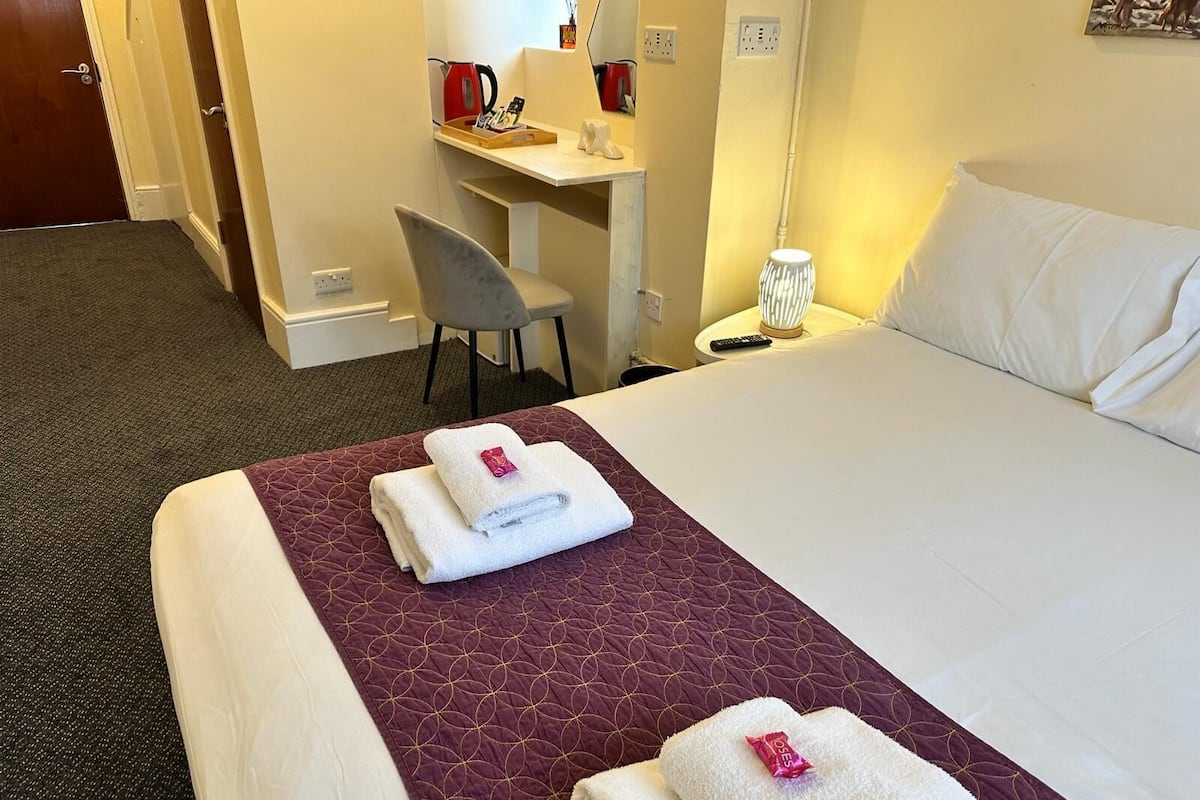 Een hotelkamer met een bed, een bureau, een stoel en een nachtkastje met een lamp.