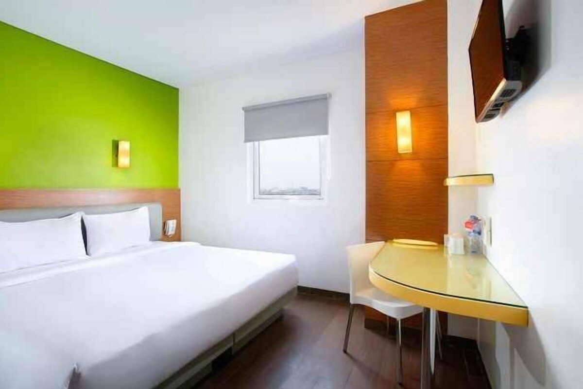 A hotel room with a bed, a desk, and a window.