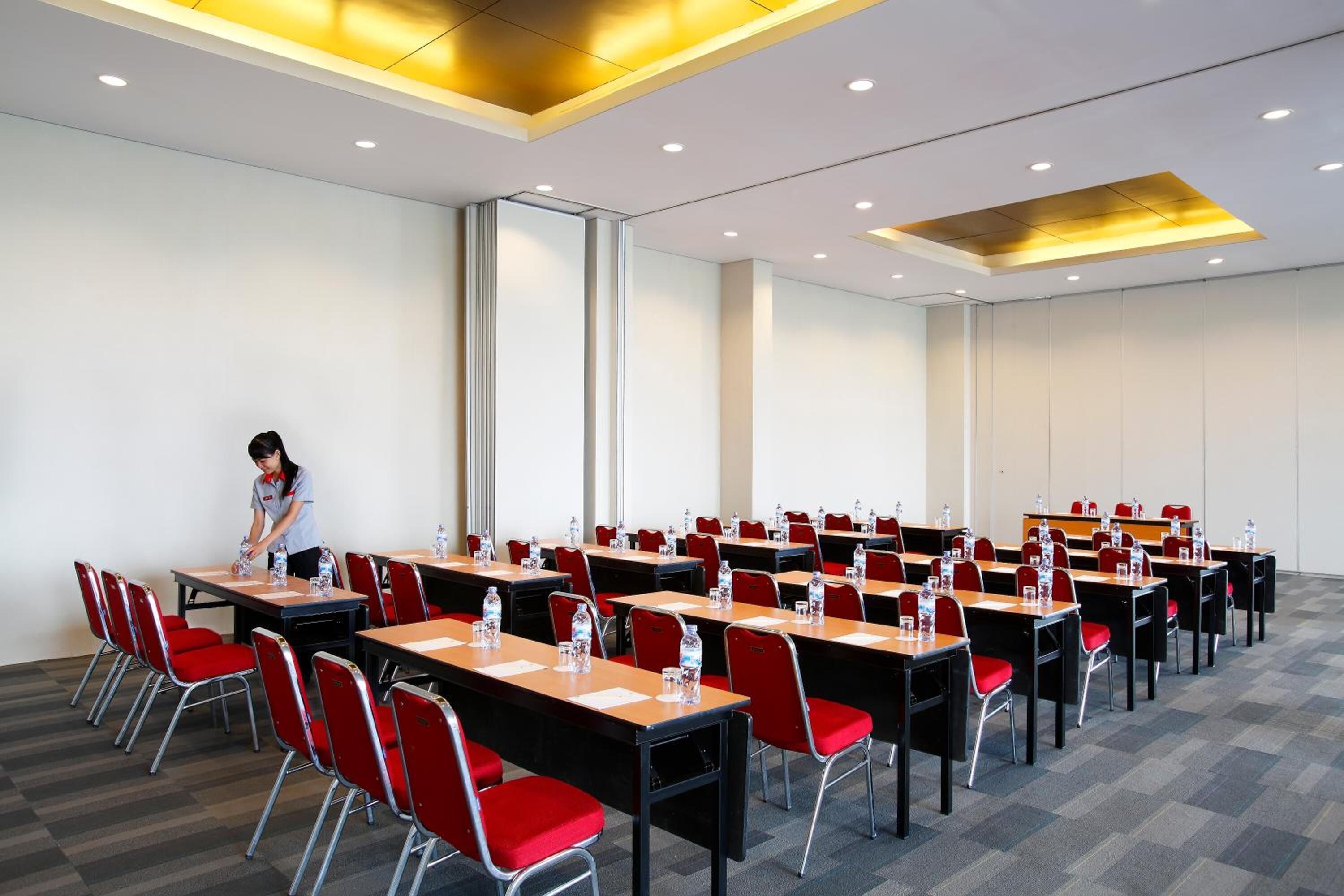 A conference room with multiple tables and chairs, equipped with water bottles and papers, and a person arranging items on one table.