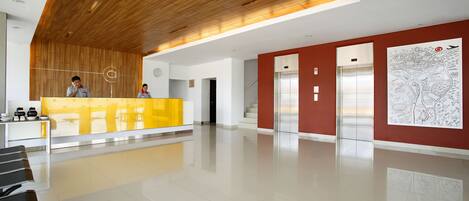 Un área de recepción moderna con techo de madera, un mostrador amarillo y dos ascensores.
