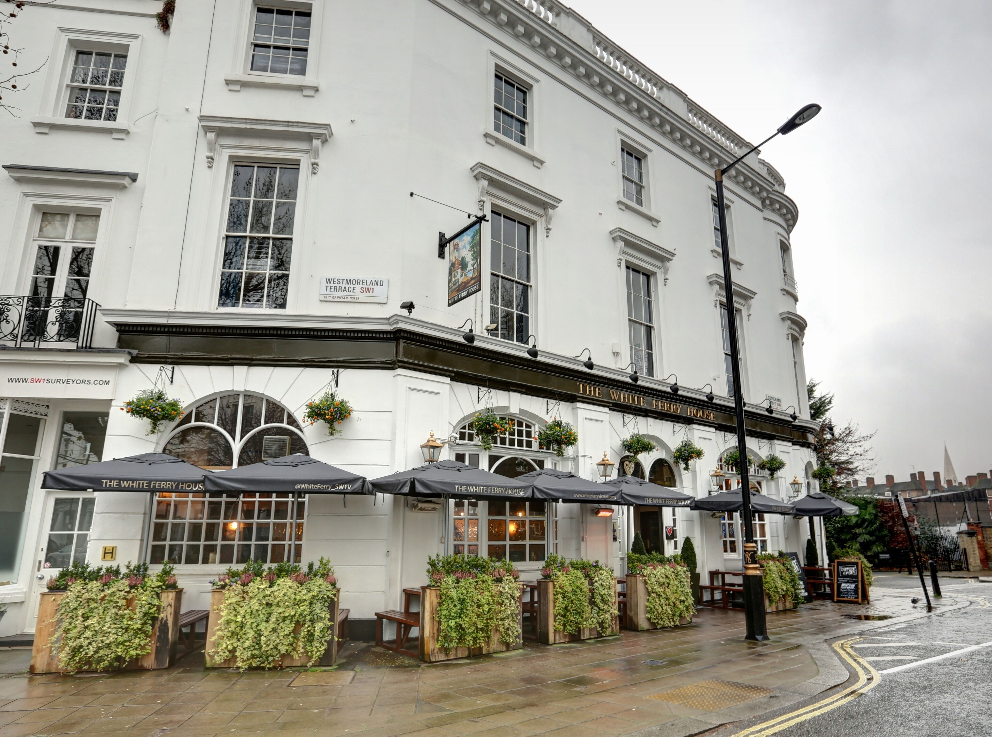 A white building with a sign reading "The White Ferry House" and outdoor seating with plants.