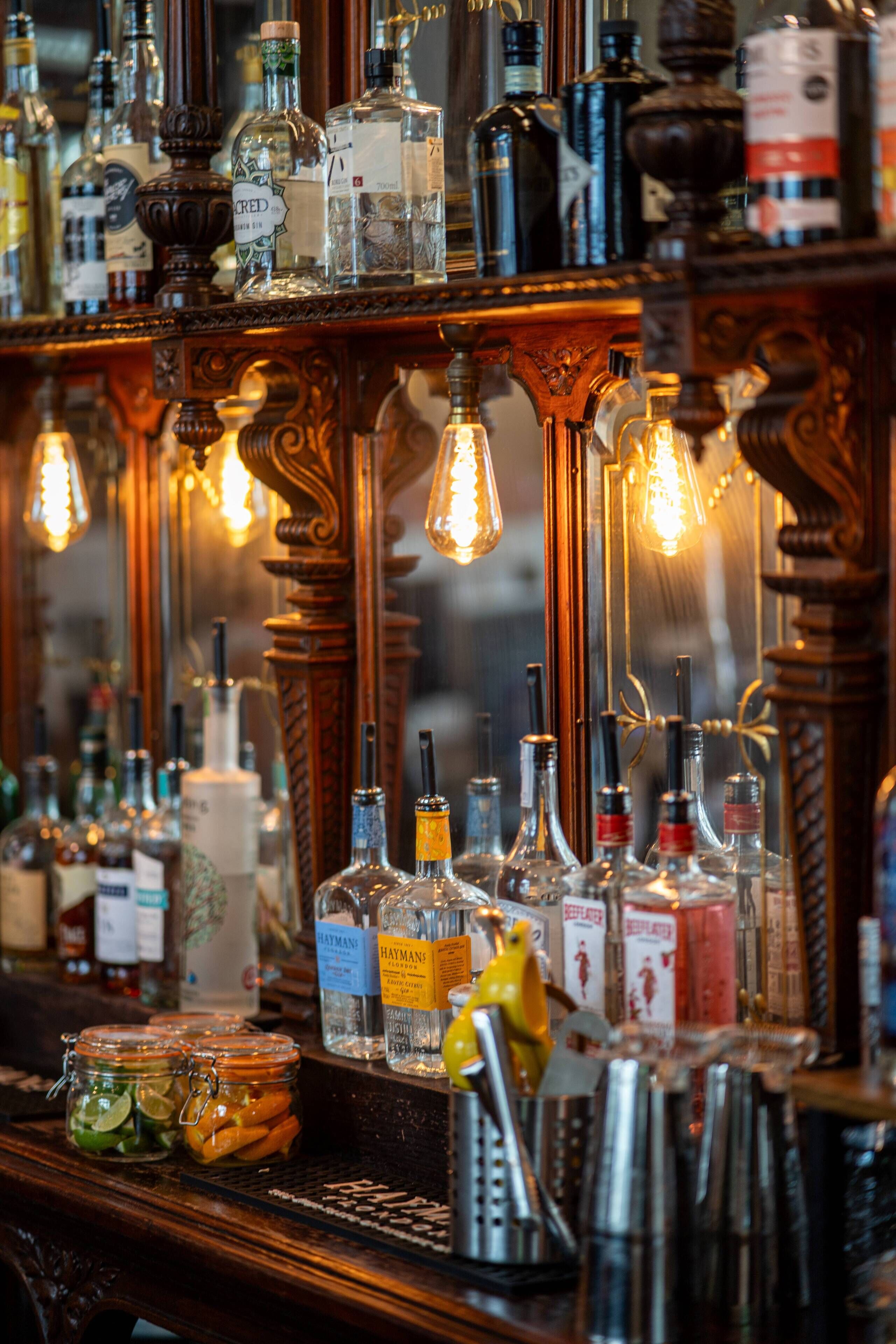 Una zona de bar con varias botellas de licor, un espejo y bombillas colgantes.