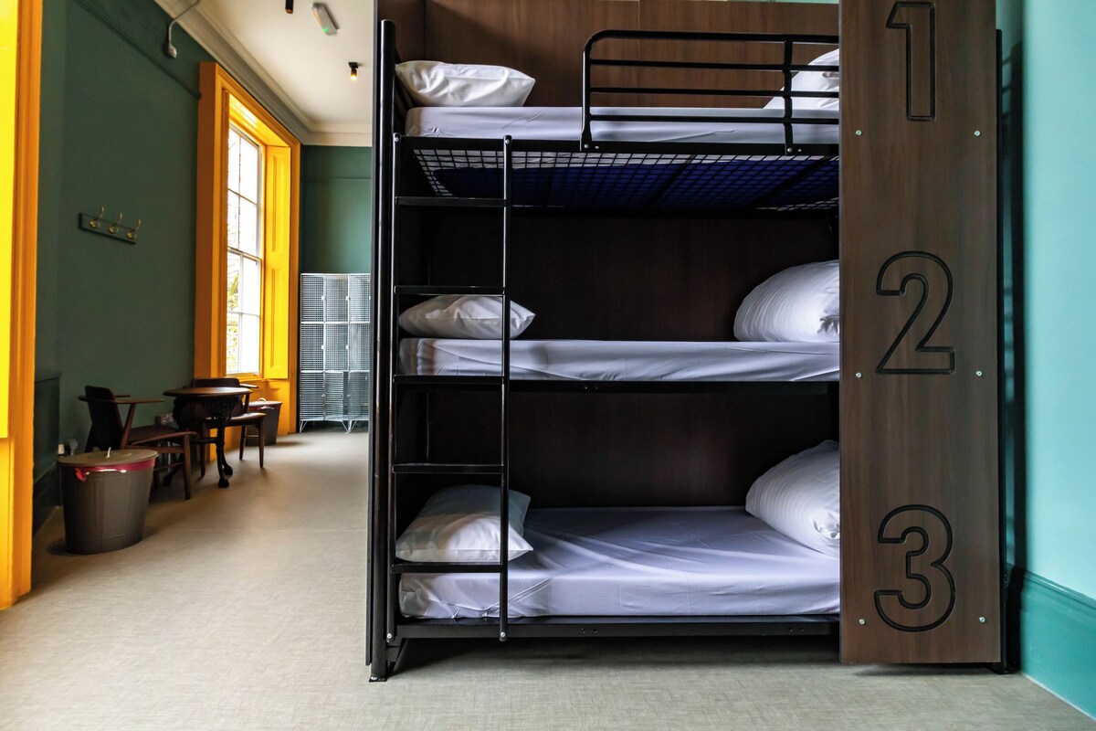 A bunk bed with three levels, a wooden door with numbers, a window, and a trash bin.