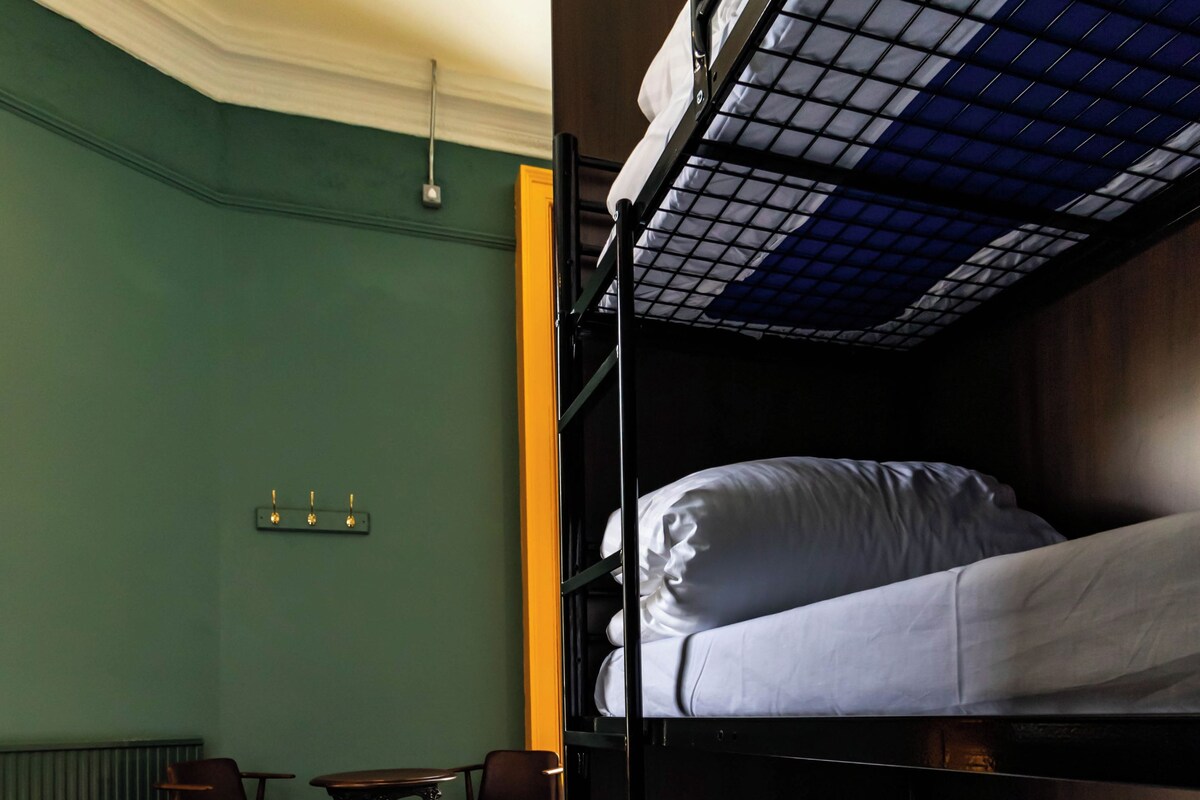 A bunk bed room with a table and chairs, a radiator, and a light fixture on the wall.