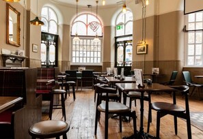 A restaurant interior with wooden tables and chairs, arched windows, and pendant lighting. - PubLove The White Ferry, Victoria - Hostel (London)
