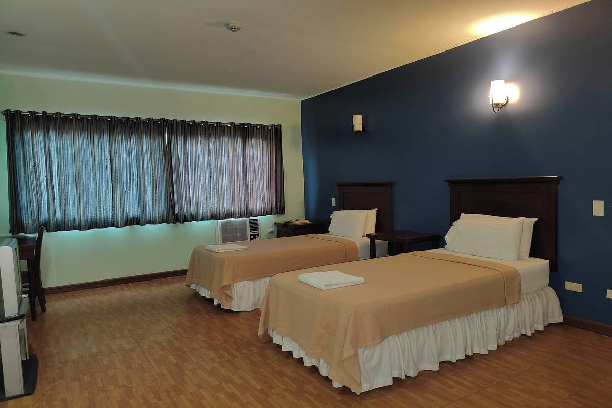A hotel room with two beds, a desk, and a window with curtains.