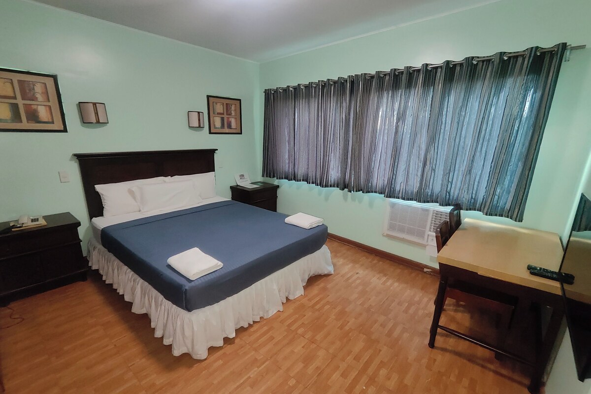 A bedroom with a bed, bedside tables, a desk, and a window with curtains.