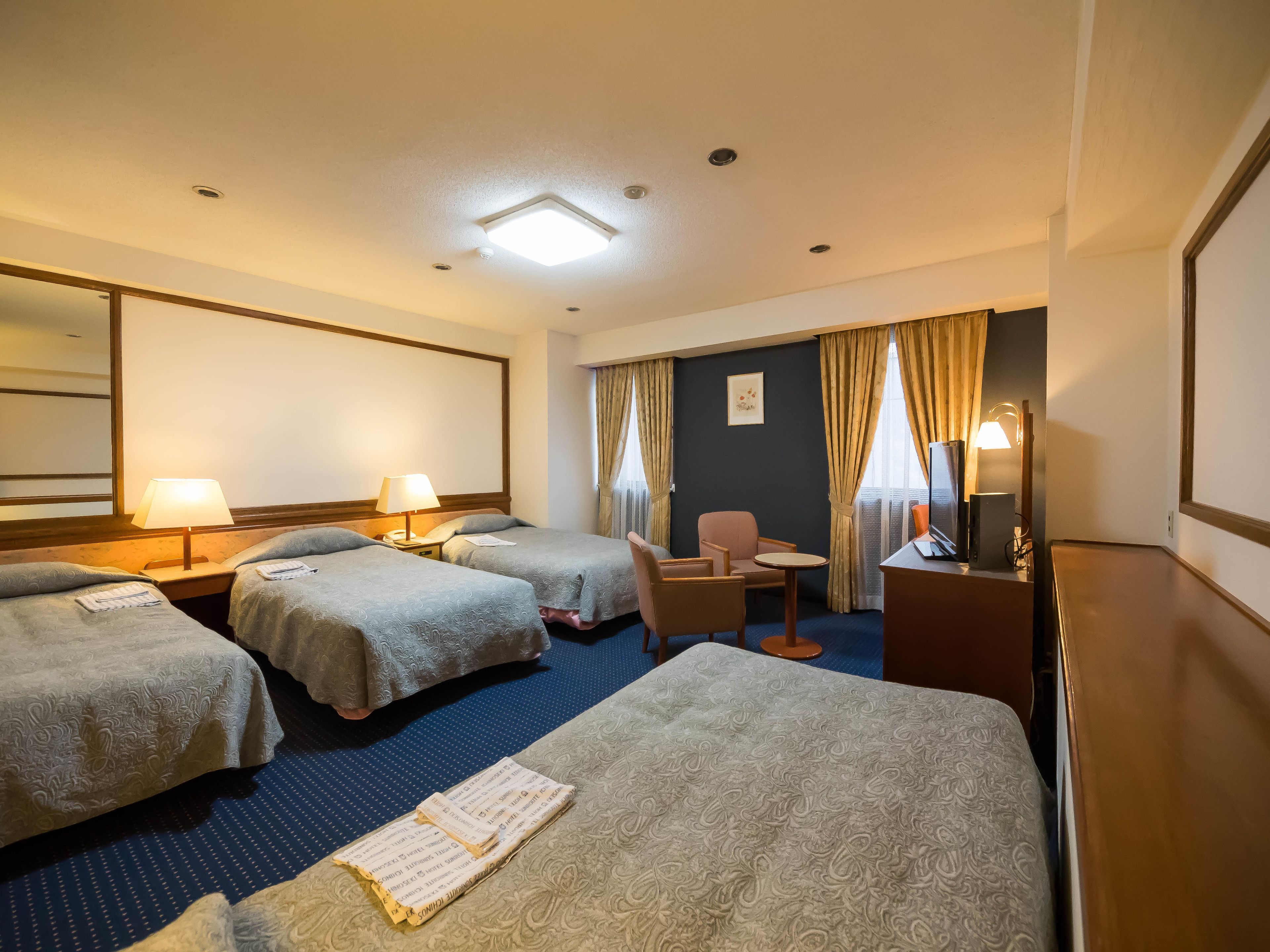 A hotel room with two beds, a desk, a chair, and a small table.