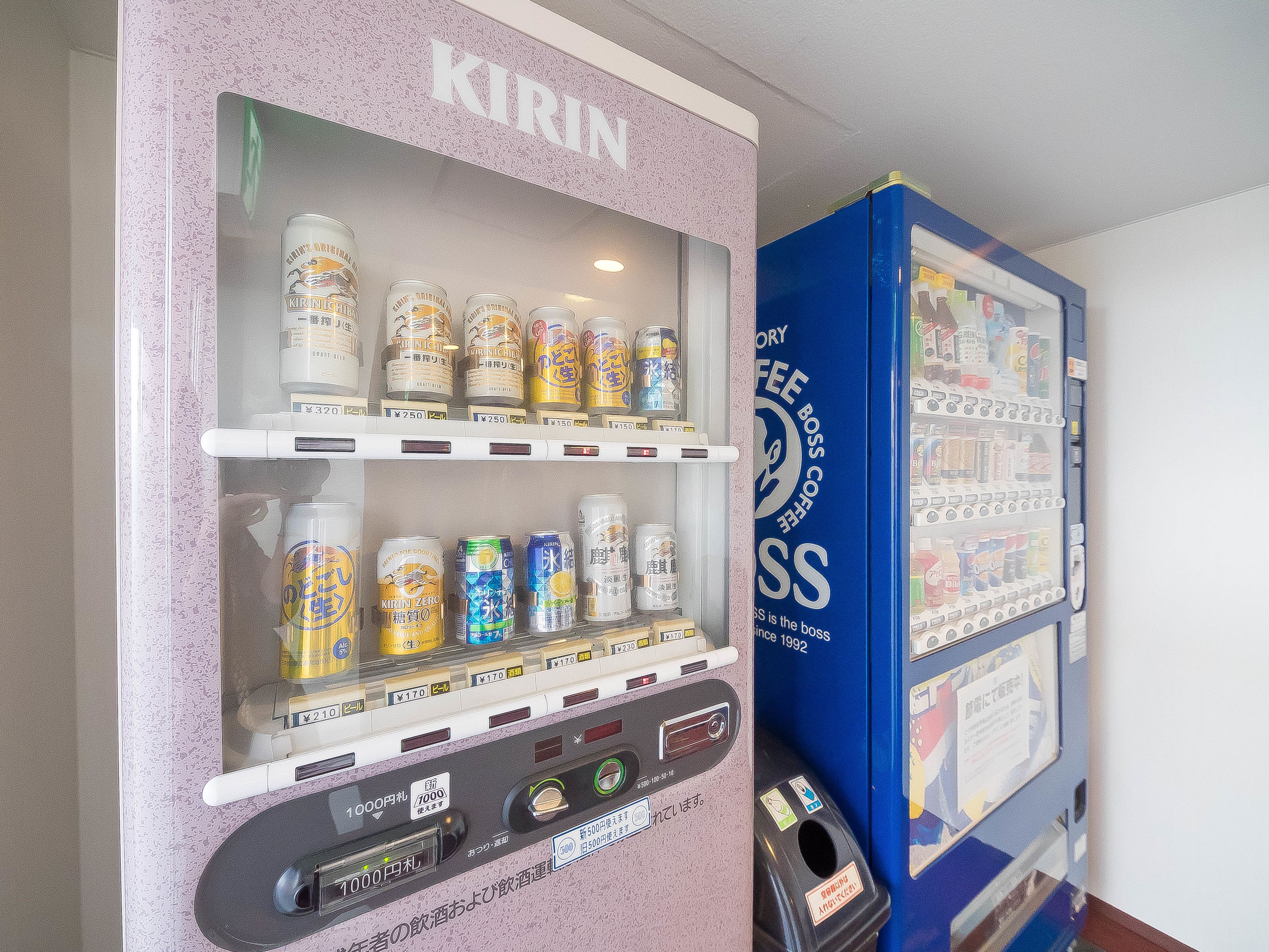 A vending machine with Kirin beer cans and a blue machine with a sign.