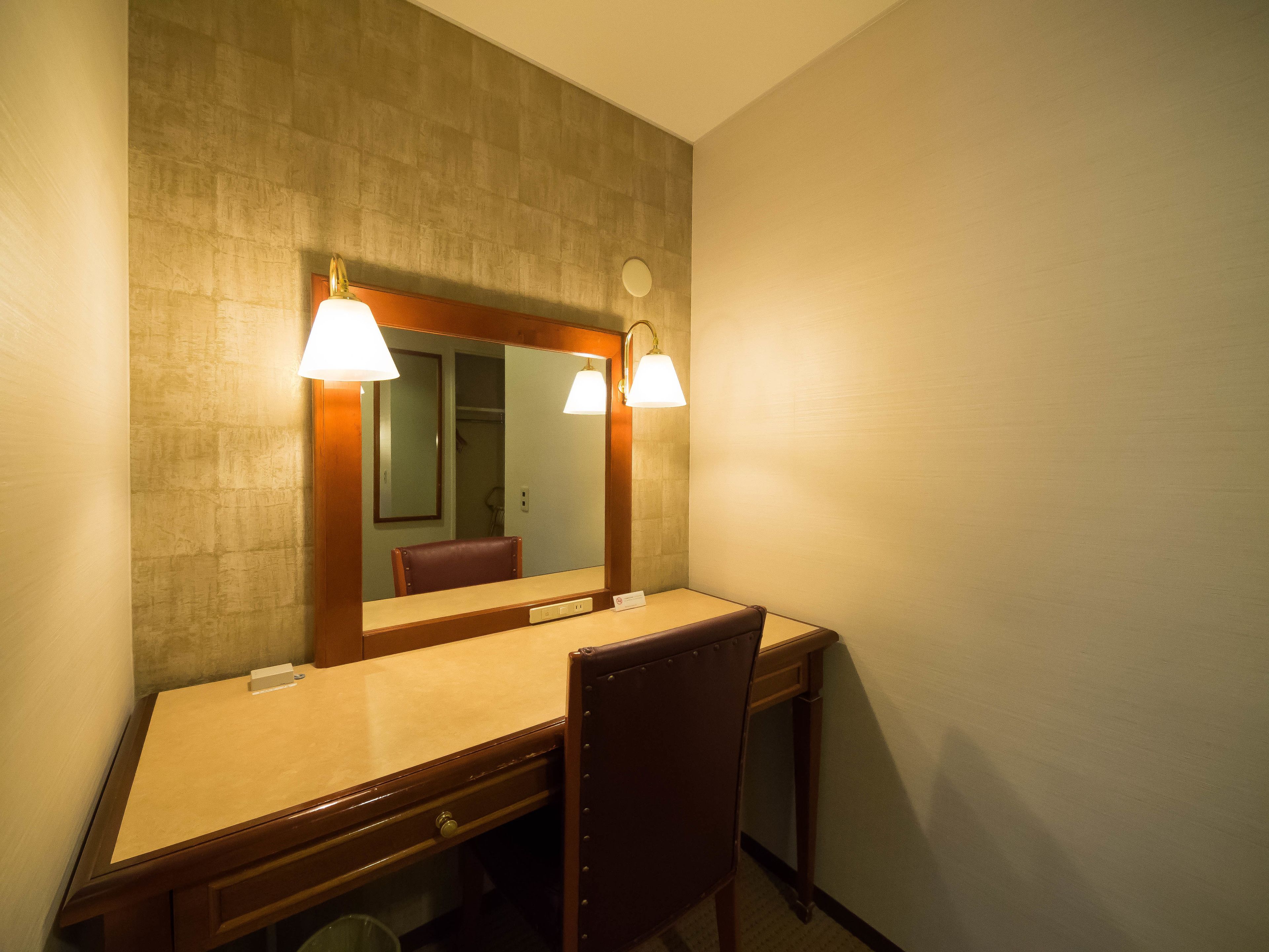 A hotel room with a wooden desk, a chair, a large mirror, and two wall-mounted lamps.
