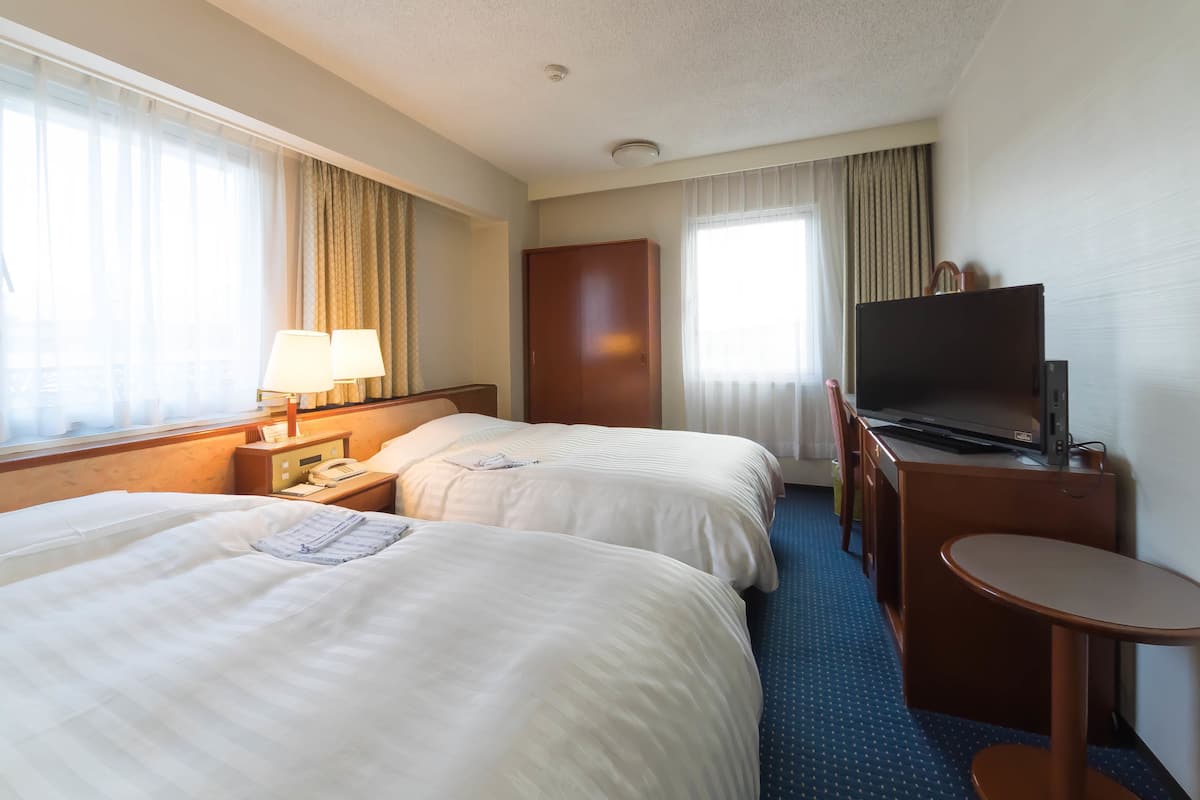 Ein Hotelzimmer mit zwei Betten, einem Schreibtisch mit Fernseher und einem kleinen Tisch.