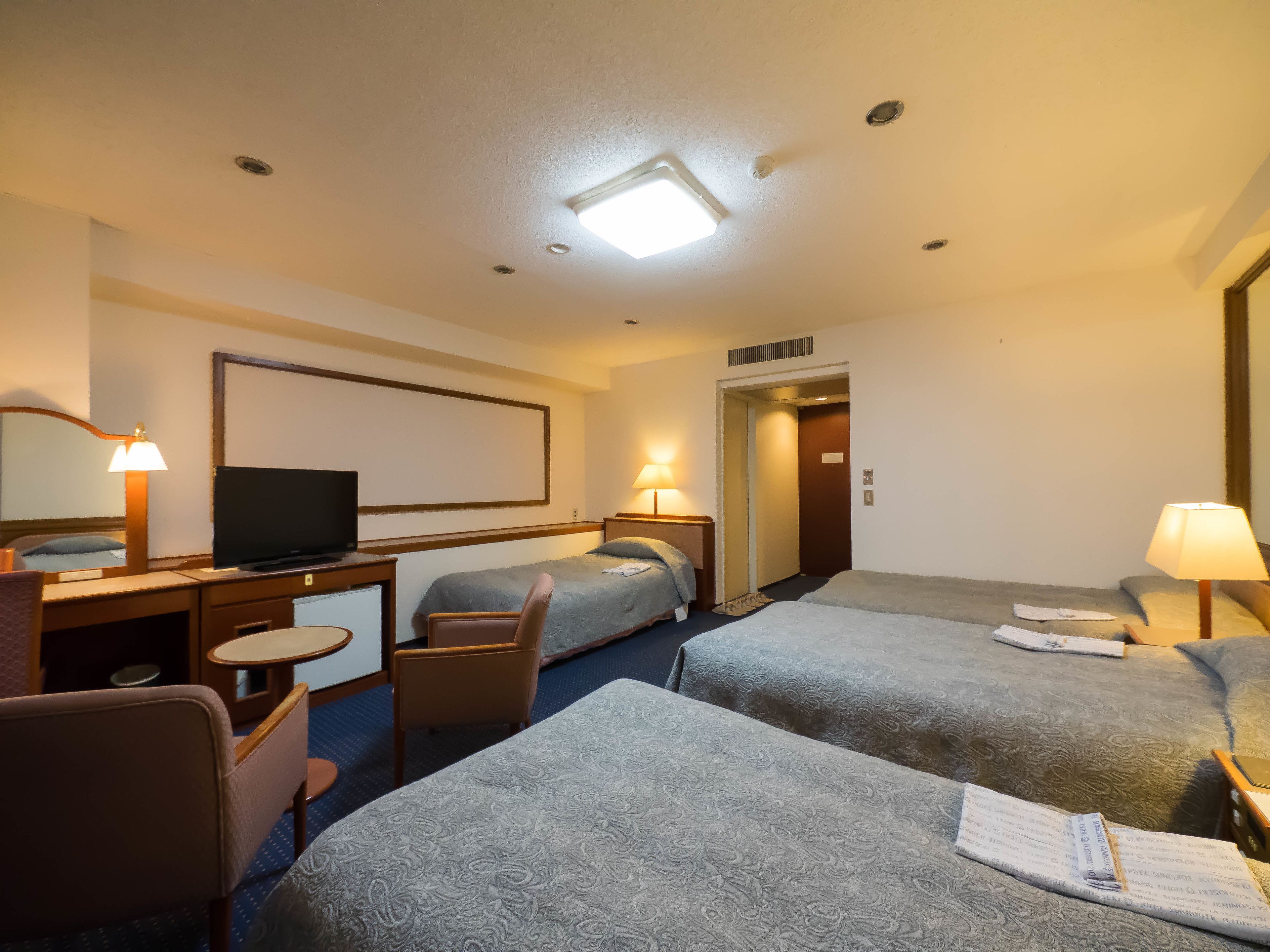 Una habitación de hotel con dos camas, un escritorio con televisor, una silla y una lámpara de escritorio.