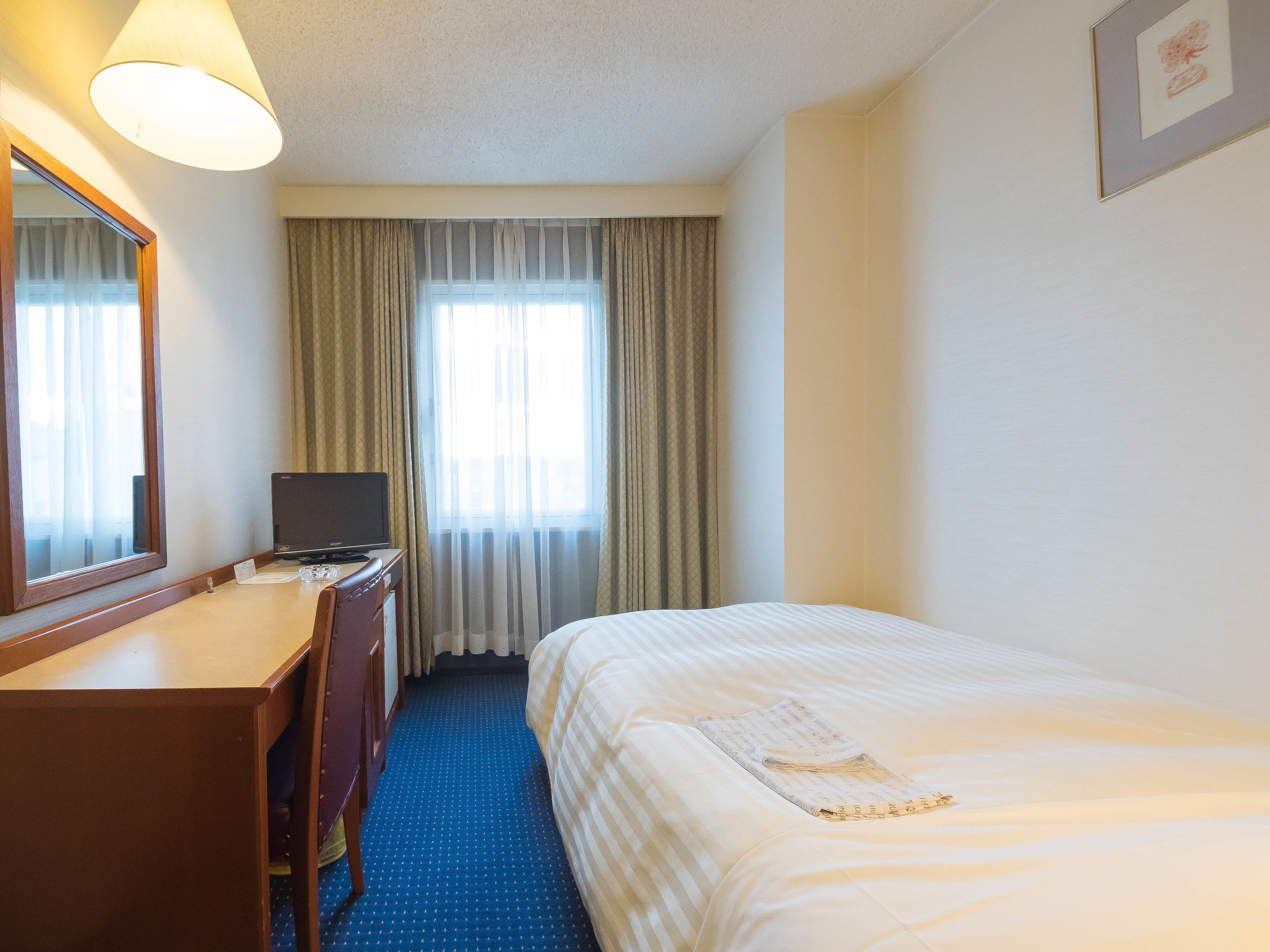 Habitación de hotel con una cama, un escritorio con computadora, un espejo y una ventana con cortinas.