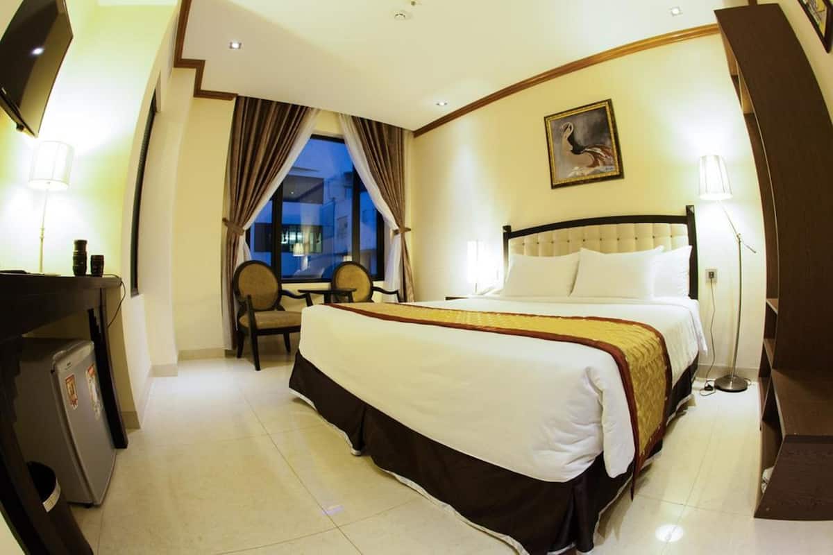 A hotel room with a bed, a desk, a chair, a TV, and a window with curtains.