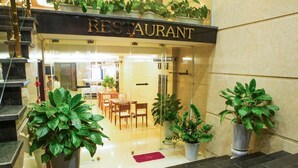 A restaurant with a modern interior, featuring a glass entrance, wooden tables, and potted plants. - The Pearl Hotel (Hanoi)