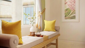 A cozy seating area with a bench, yellow pillows, a white vase with flowers, and a teapot on the table. - The Pearl Hotel (Hanoi)