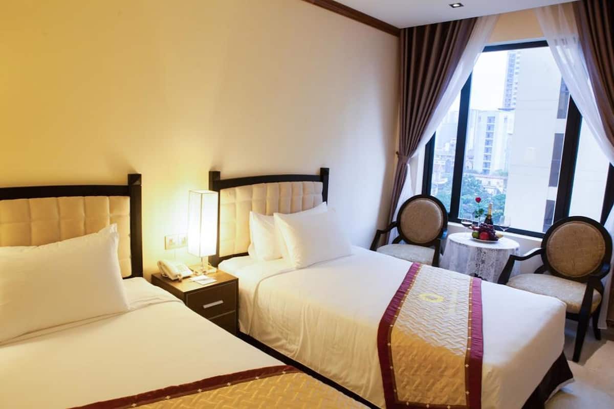 A hotel room with two beds, a small table with chairs, and a window with curtains.