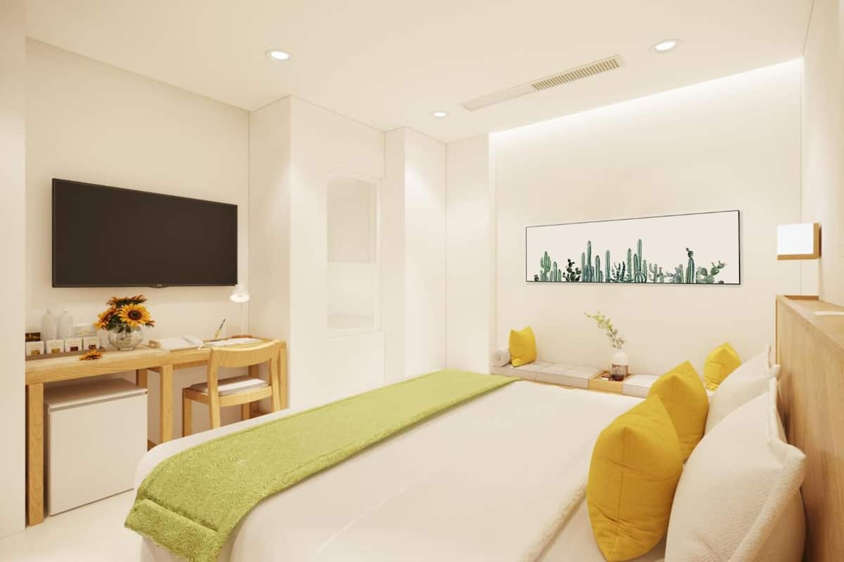 A modern hotel room with a bed, a desk, a flat-screen TV, and a cactus-themed artwork on the wall.