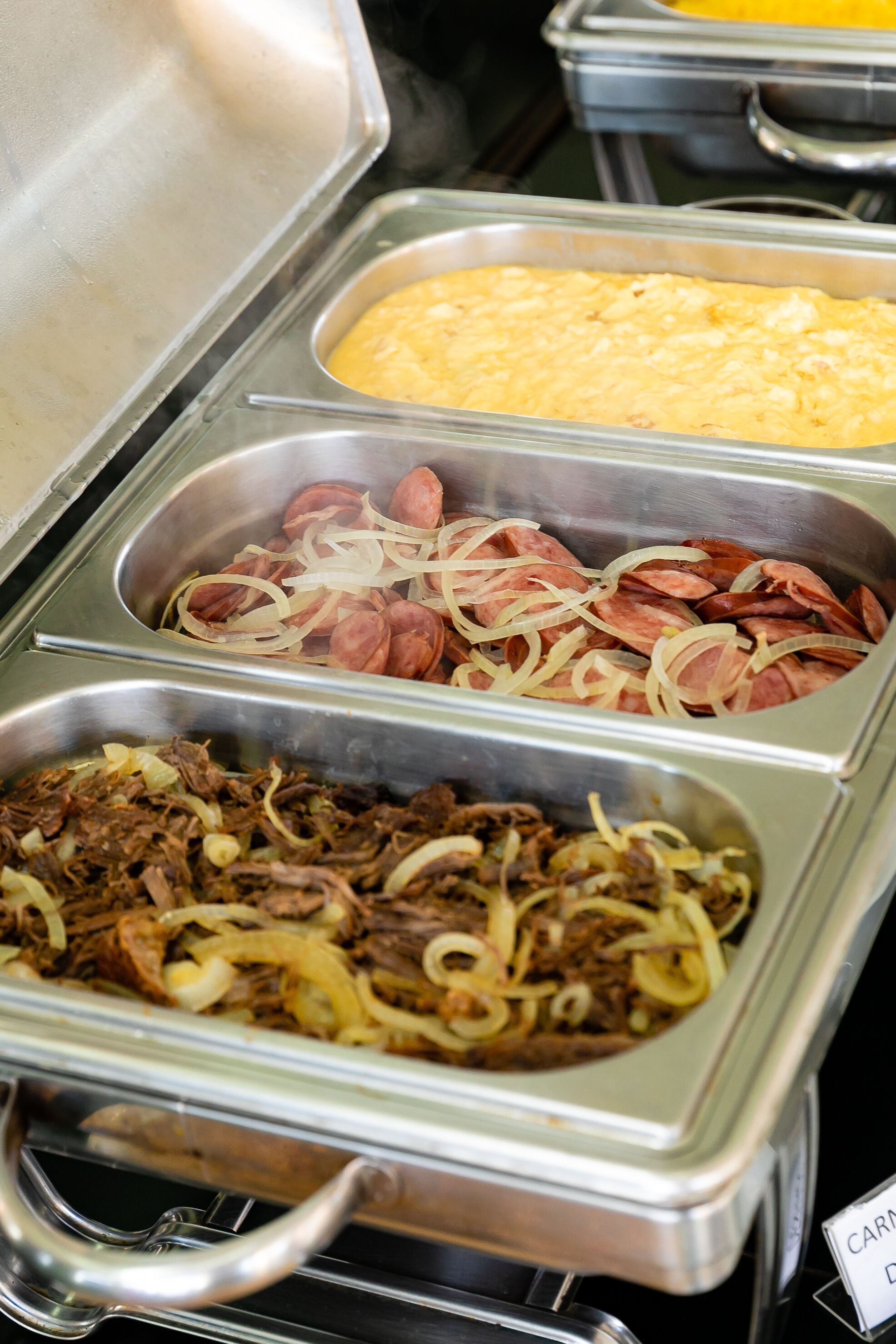 Un buffet proposant divers plats, notamment des saucisses, de la viande effilochée et un plat en gratin.