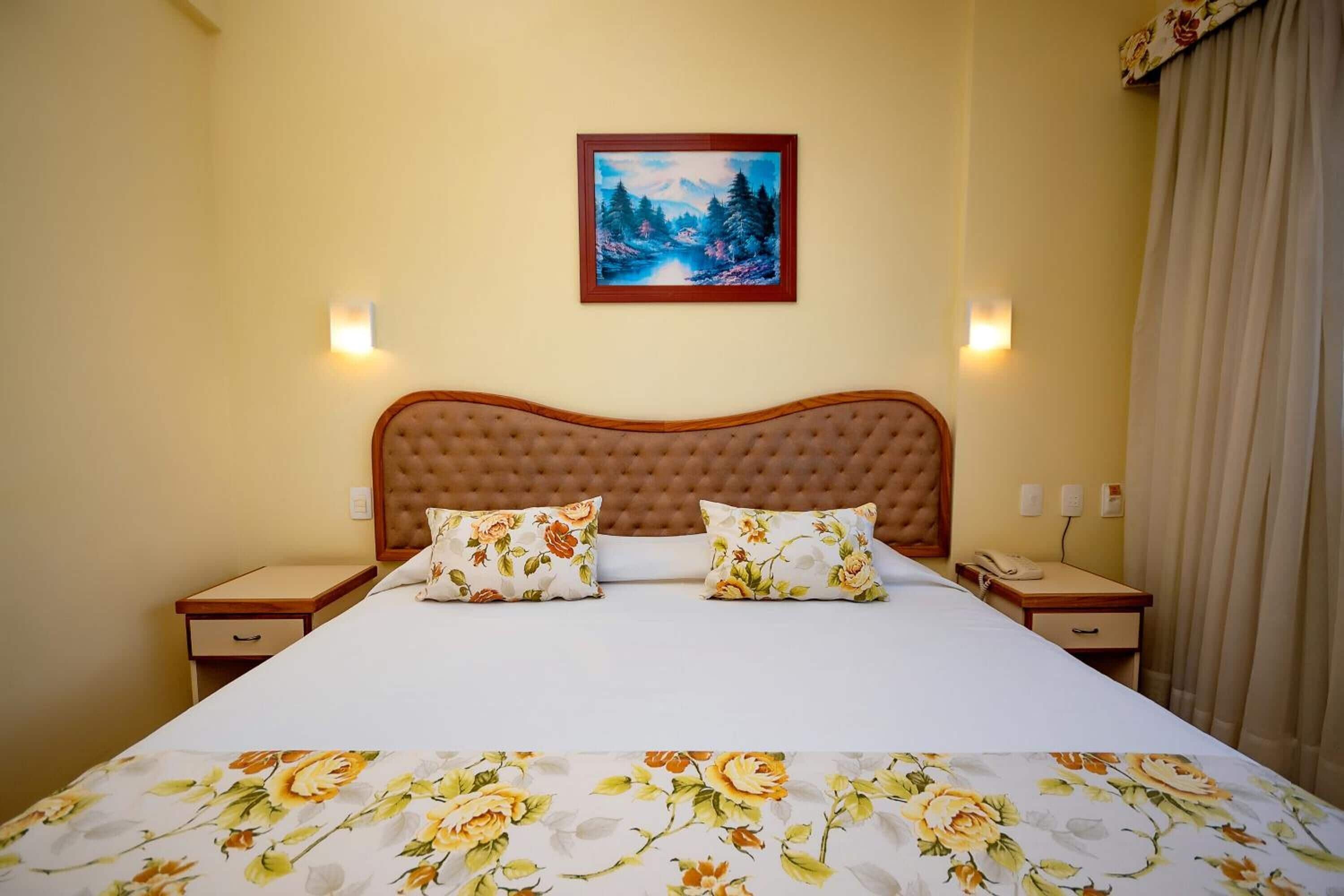 Une chambre d’hôtel avec un grand lit, une literie à motifs floraux, un tableau au-dessus du lit et deux tables de chevet avec des lampes.