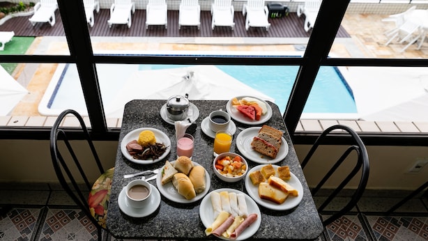 Una mesa de desayuno con diferentes alimentos y vistas a una piscina y sillones de descanso.