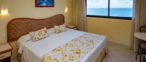 Een slaapkamer met een groot bed, een nachtkastje, een stoel en een raam met uitzicht op zee.