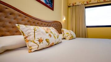 Una cama con almohadas estampadas con motivos florales, cabecera capitonada y ventana con cortinas.