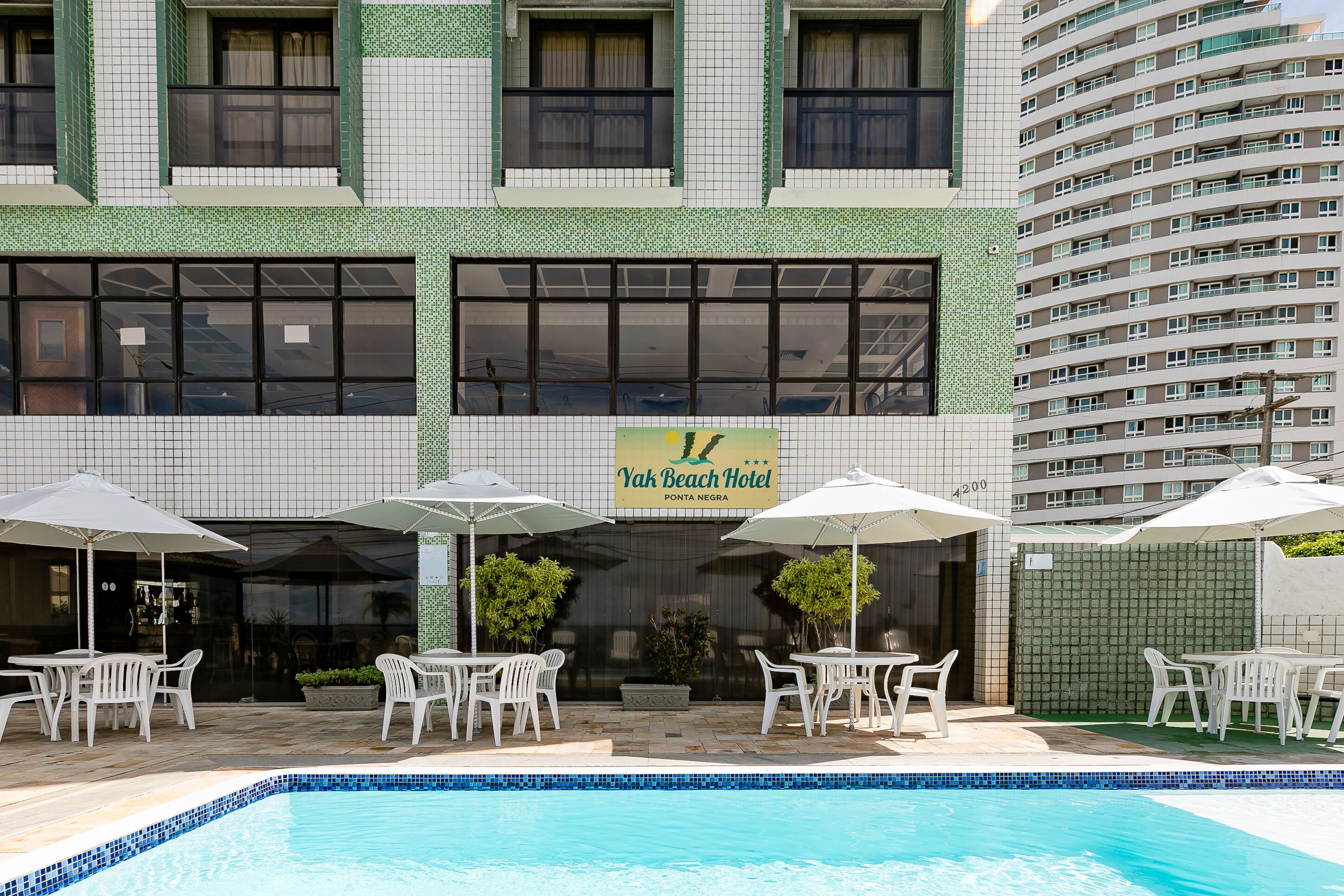 A hotel with a pool area, outdoor seating, and a sign for Yak Beach Hotel.