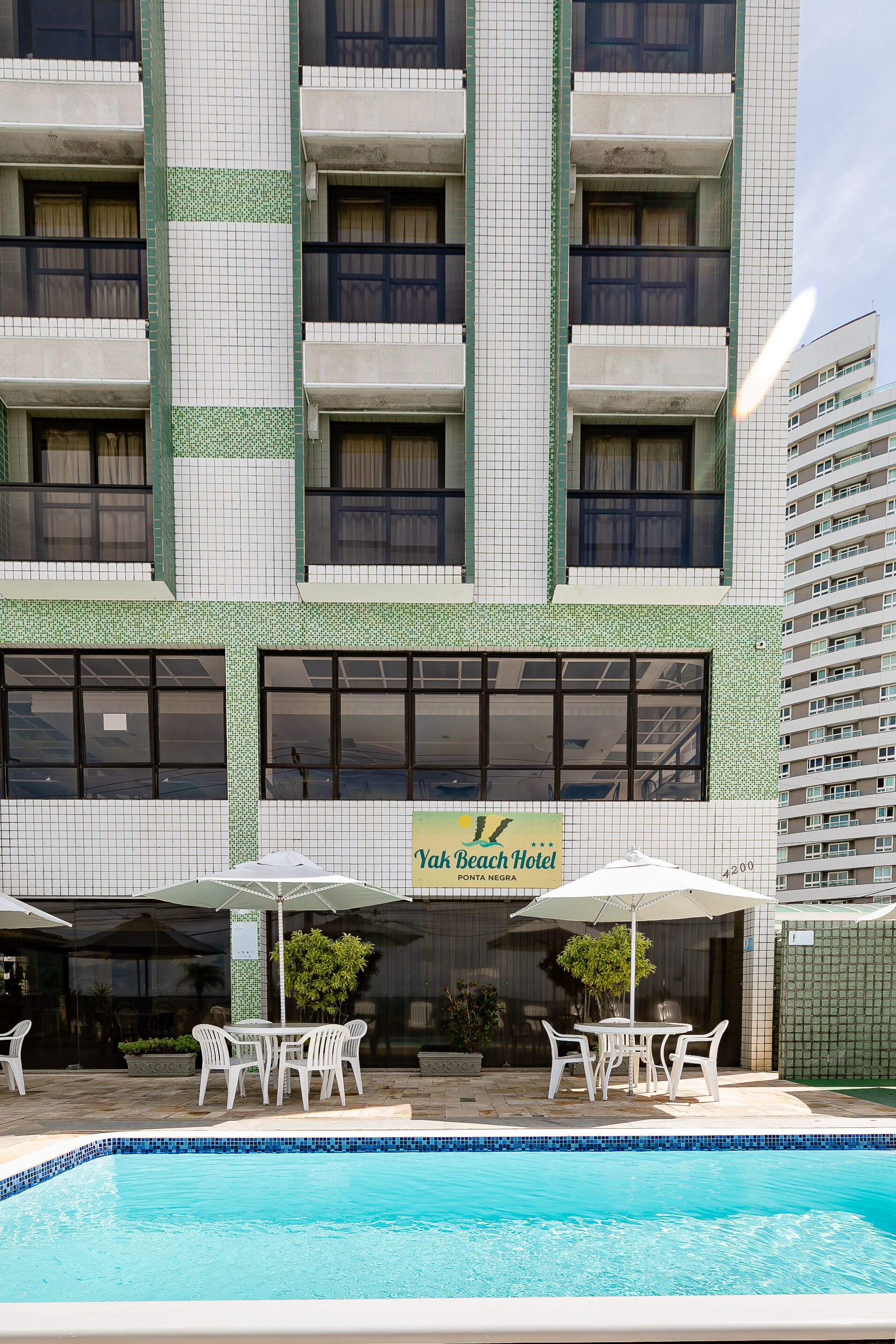 A hotel building with a pool area, outdoor seating, and a sign for Yah Beach Hotel.