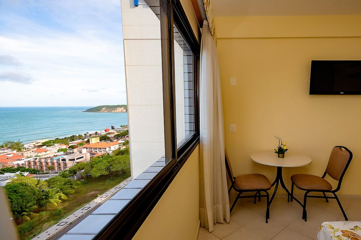 A balcony with a view of the sea, a table with two chairs, and a TV mounted on the wall.