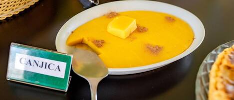 Uma tigela de sopa com o rótulo 'CANJICA', com uma colher e um pedaço de manteiga por cima.