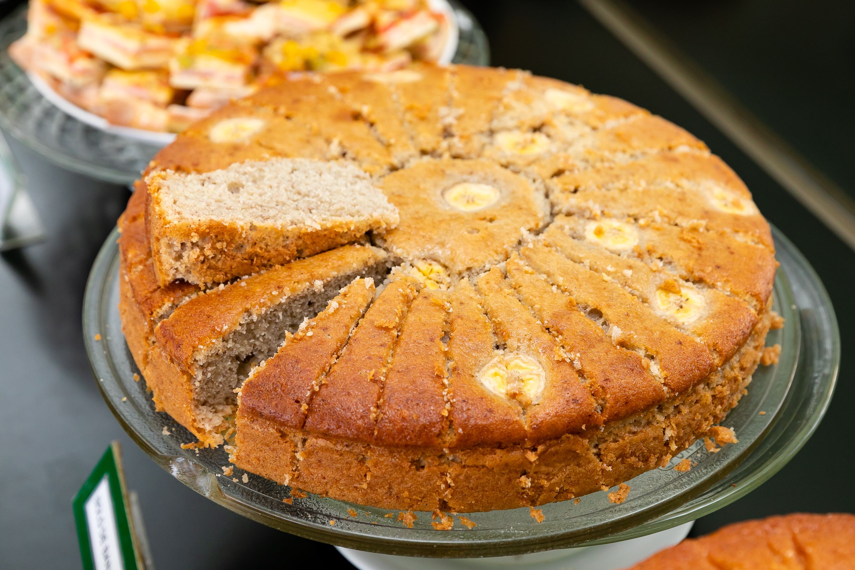 A round cake with a golden-brown crust, sliced into triangular pieces, displayed on a glass cake stand.