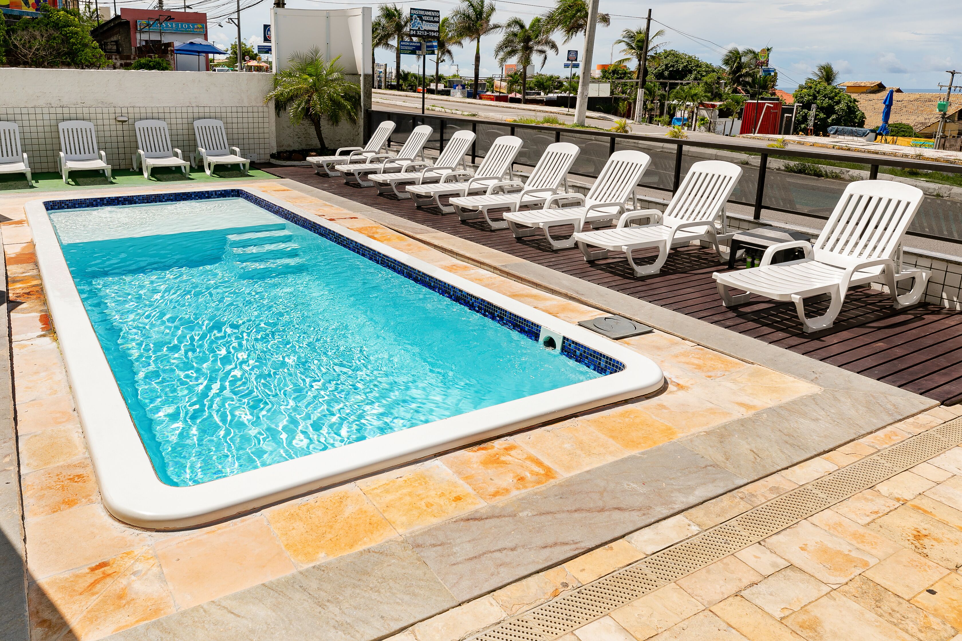 Une piscine rectangulaire bordée de carreaux, entourée de chaises longues blanches et d’une terrasse également carrelée.