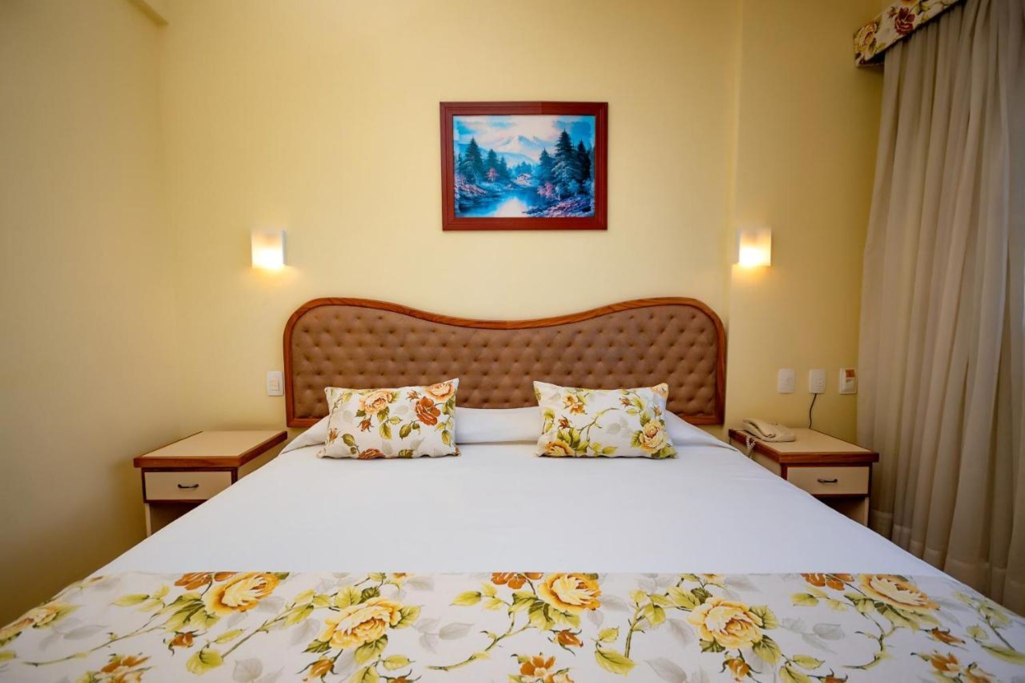 A hotel room with a large bed, two nightstands, a painting on the wall, and a telephone on one of the nightstands.