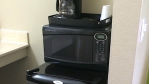 A black refrigerator with a microwave on top, a coffee maker, and a white cup. - California Inn & Suites Adelanto US 395 (Adelanto)
