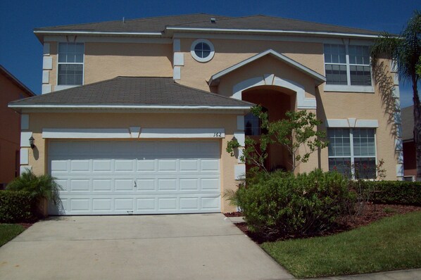 A two-story house with a white garage door, a small circular window above the garage, and a number '162' on the garage door.