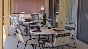 Een terras buiten met ronde tafels en stoelen, plafondventilatoren en uitzicht op de straat.