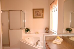 A bathroom with a bathtub, a shower, a vanity with a mirror, and a framed picture on the wall.