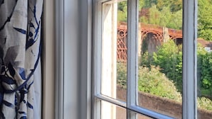 A window with a view of a red bridge and greenery. - Ironbridge View Townhouse (Telford)
