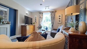 A living room with a sofa, a television, a wooden cabinet, and a window with curtains. - Ironbridge View Townhouse (Telford)