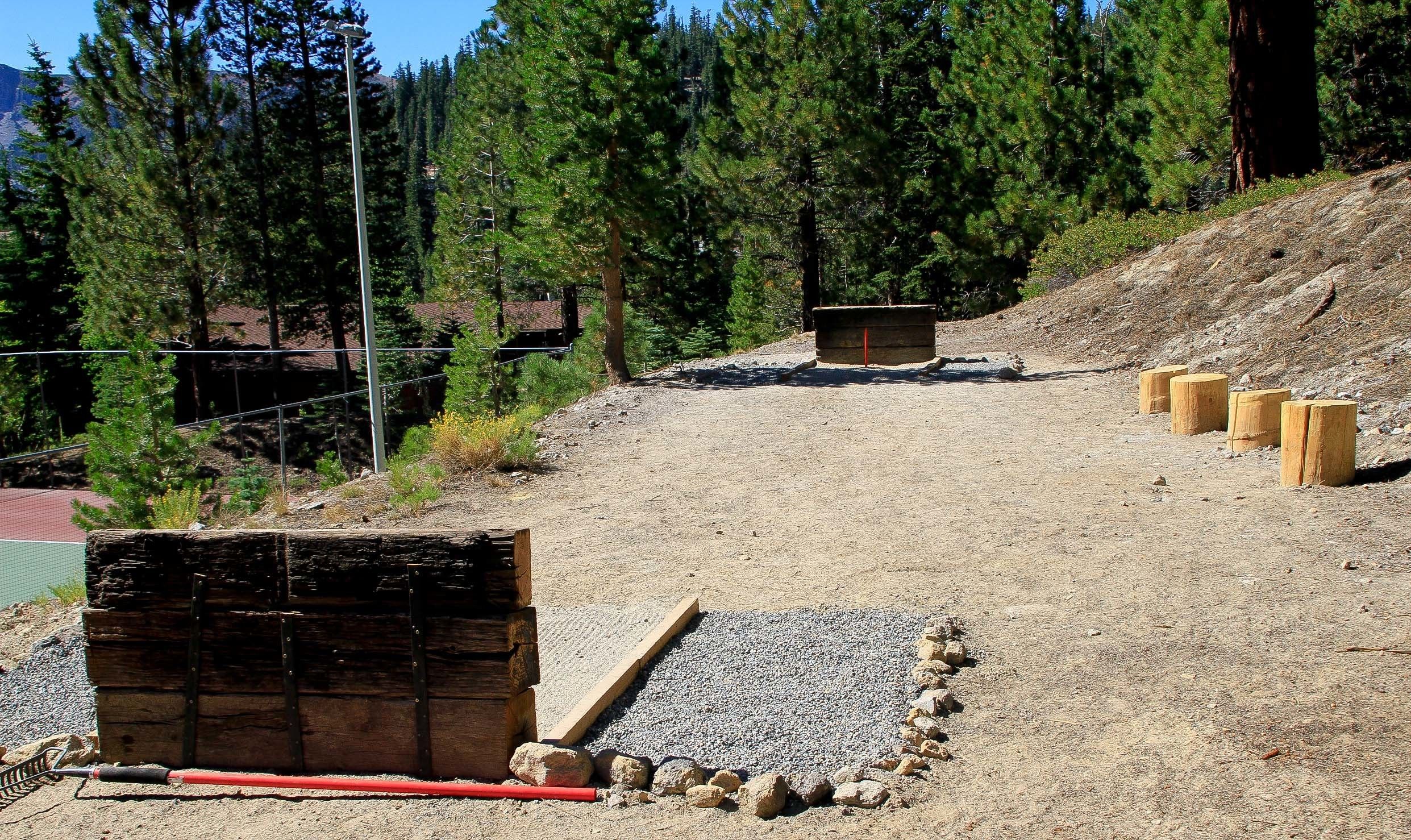 Un sendero de grava con estructuras de madera y una cerca metálica en un área boscosa.