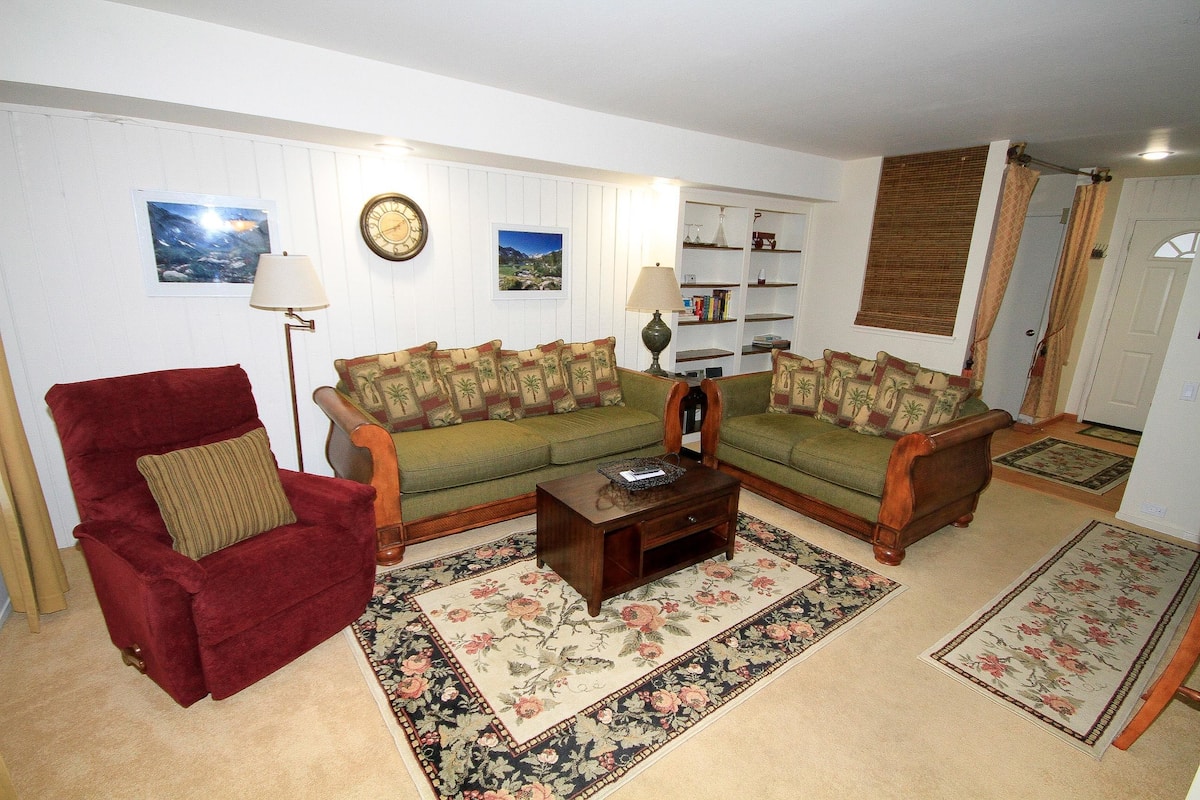 A living room with a red armchair, two green sofas, a wooden coffee table, and a floral area rug.