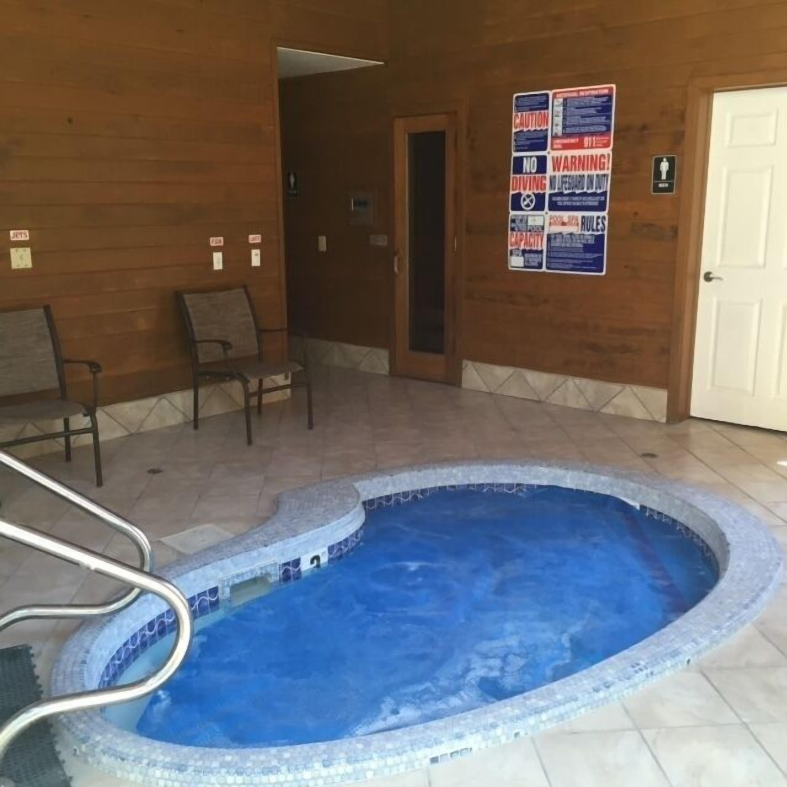 Una piscina pequeña techada con borde de azulejos, paredes de madera y una puerta con un letrero.