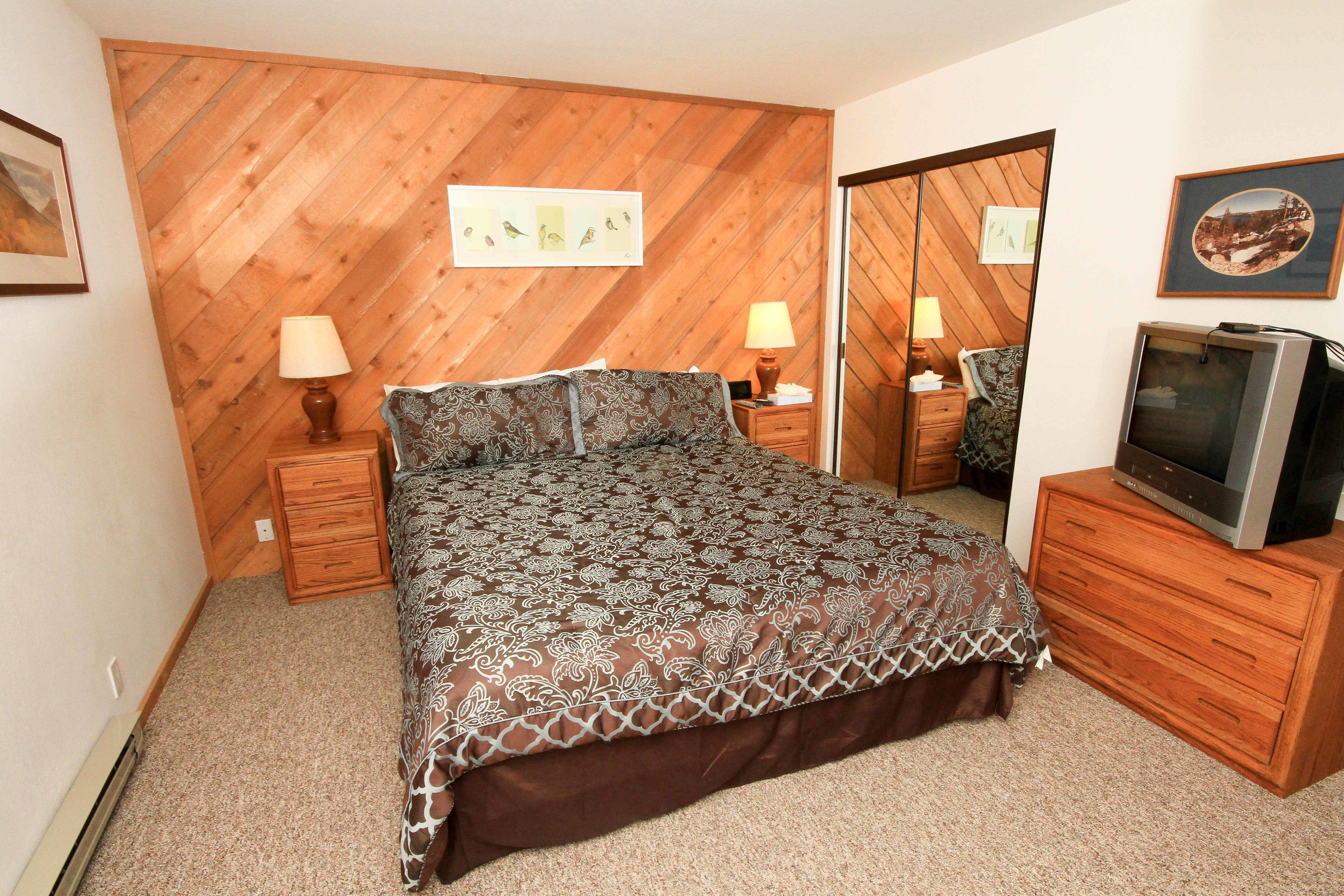 Un dormitorio con una cama, dos mesitas de noche con lámparas, un aparador, un televisor y un panel de pared de madera.