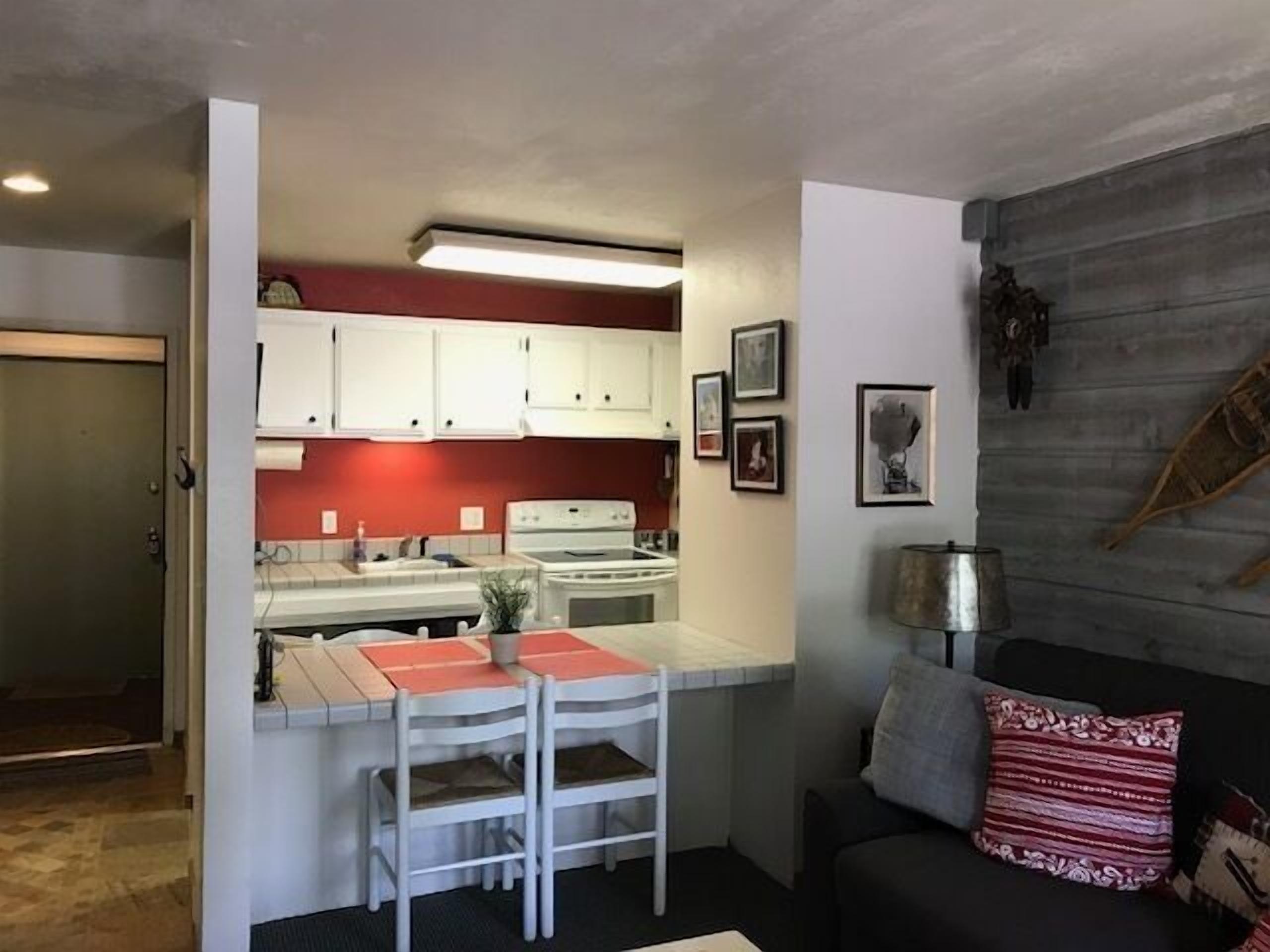 A compact kitchen with white cabinets, a stove, and a dining area with a table and chairs.
