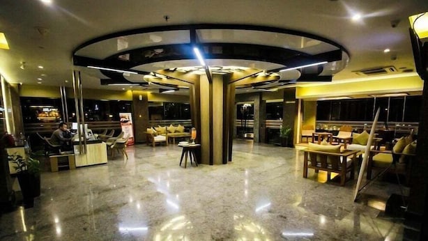 Um lobby de hotel moderno com um design central circular, áreas de estar e um balcão de recepção.