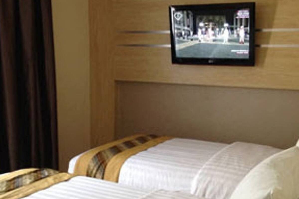 A hotel room with two beds, a television mounted on the wall, and a window with curtains.