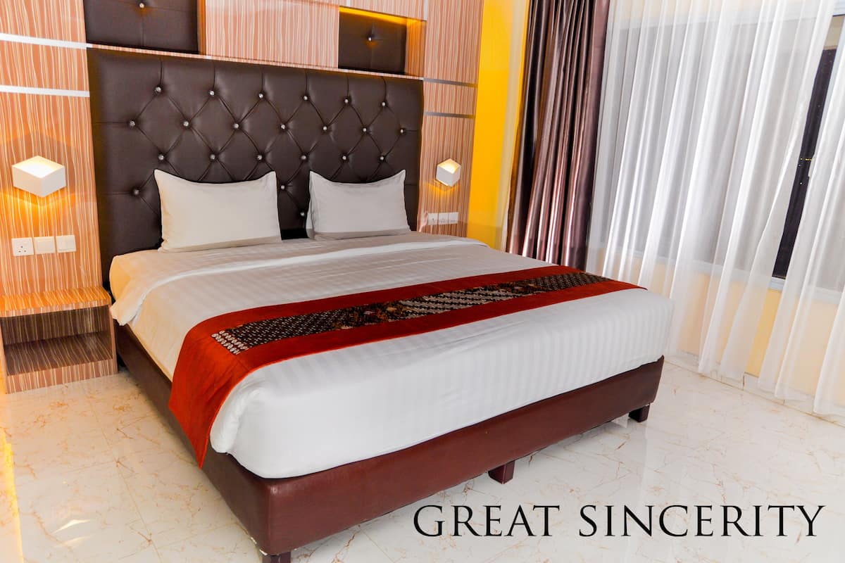 A hotel room with a large bed, a tufted headboard, and a red throw blanket.