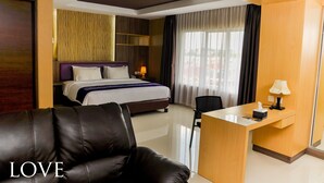 Quarto de hotel com cama, escrivaninha, poltrona de couro e uma janela grande com cortinas.