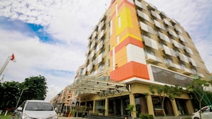 Um hotel com várias andares, fachada geométrica marcante, entrada de vidro e um mastro com bandeira.